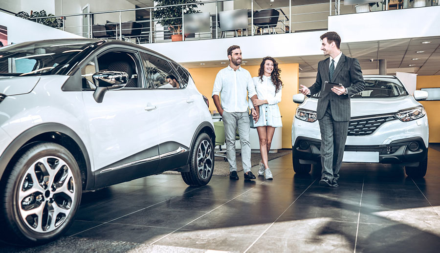 Junges Pärchen wird vom Berater durch ein Autohaus geführt